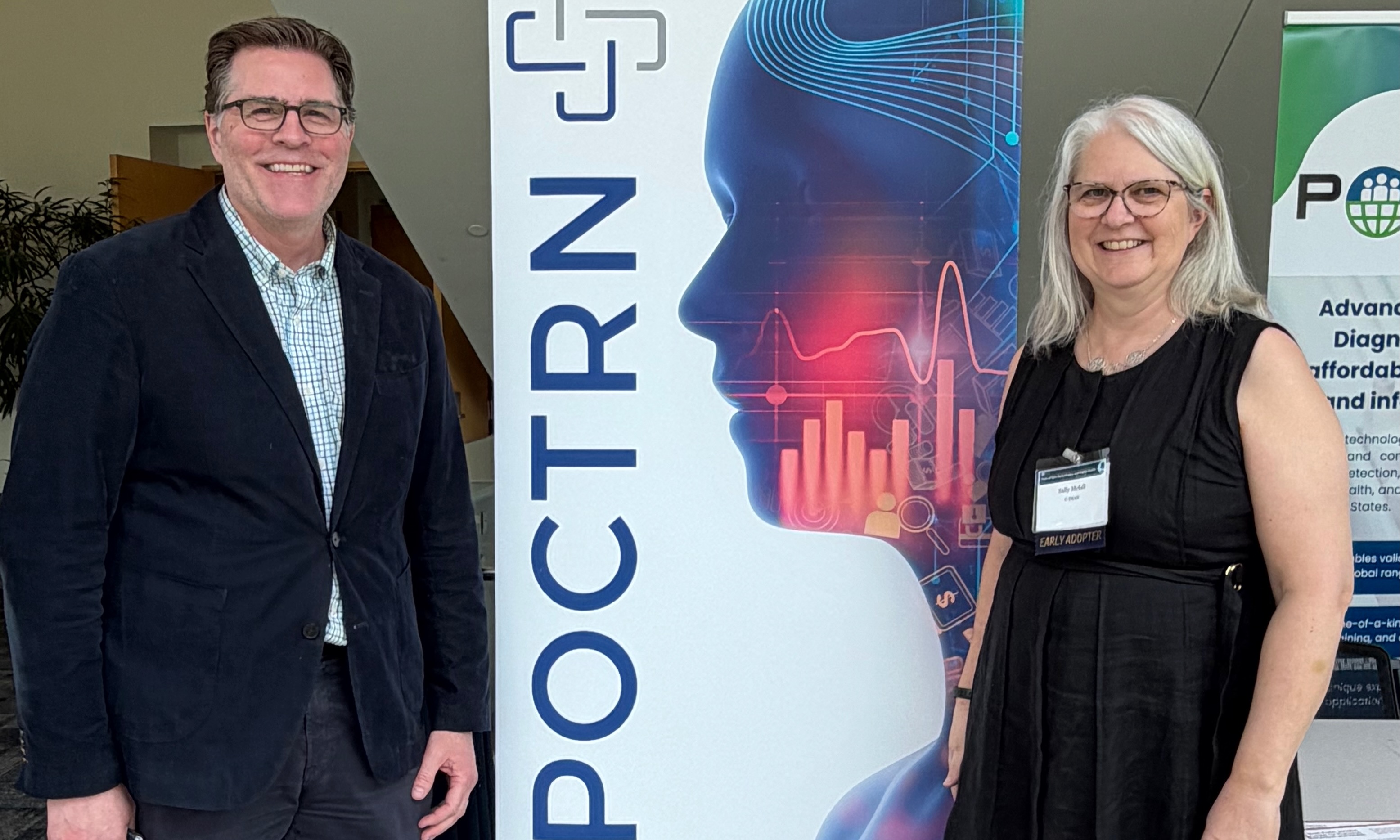 Chad Achenbach and Sally McFall stand in front of a POCTRN sign