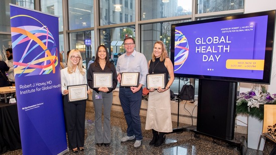 Four Global Health Day award winners holding certificates and standing in front of Global Health Day signs