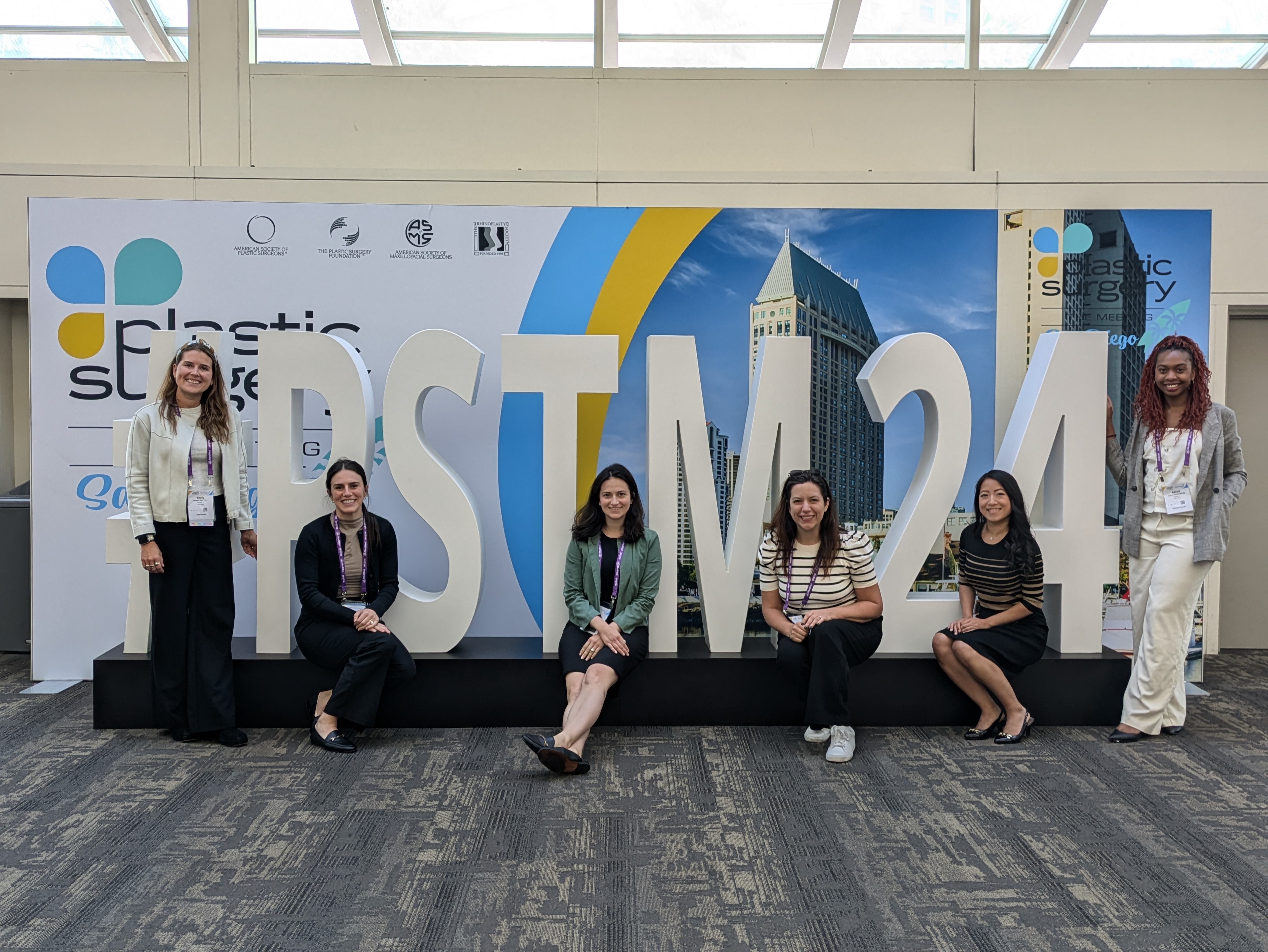 Surgical residents and physician assistants sitting and standing on a life-size sign that says PSTM 24