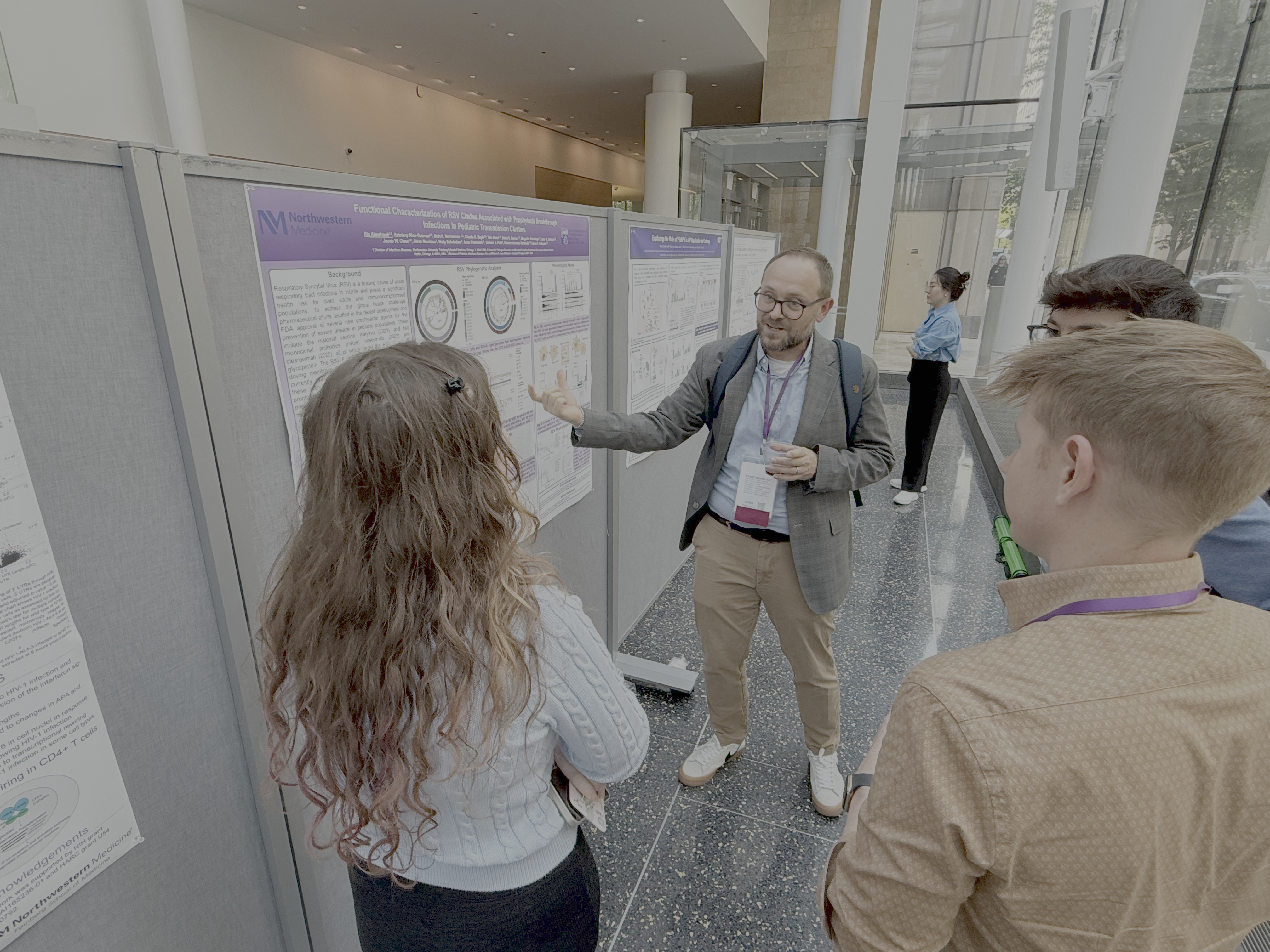 Three event attendees listen to a presentation in front of the poster and presenter