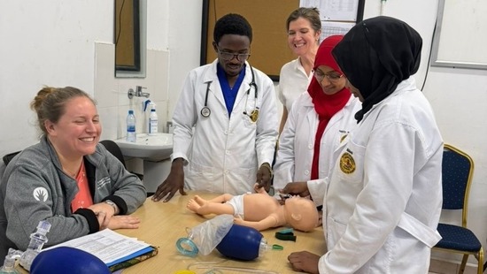 A medical team stands around a simulation doll on a table